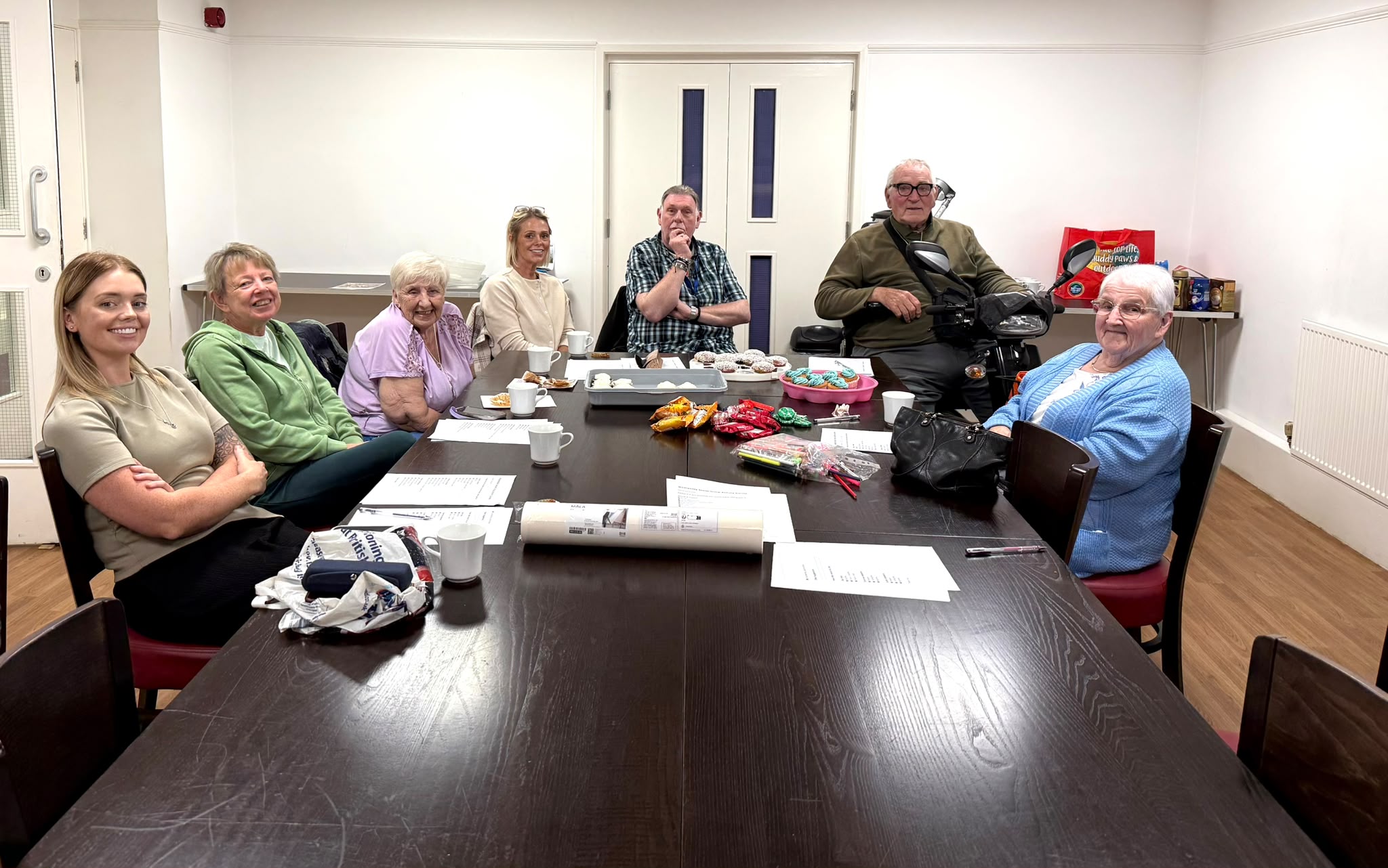 A group of people, younger and older, sitting around a long table, smiling.